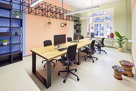 The walls in this office are painted in three colors: green, orange, and blue. In the middle stands a long wooden table, and around it are several black IN swivel chairs.
