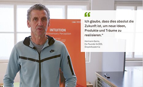 A man named Hermann Gams, co-founder and CEO of DreamAcademia, stands in a bright room in front of an orange display. Next to him is his quote: “I believe this is absolutely the future for realizing new ideas, products, and dreams.”