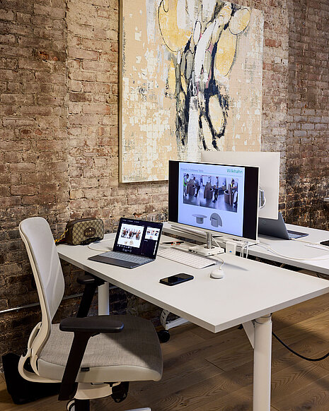 Two white tables stand in front of a brown brick wall. In front of one of the tables is a gray-and-white IN swivel chair.