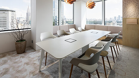 Occo chairs with beige or white seat shells are arranged around a long white conference table. The conference room has many windows and is generally decorated in shades of beige.