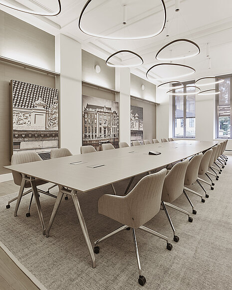 The photo shows a spacious, bright conference room with a long table and beige upholstered swivel chairs on casters. These are the Yonda conference chairs. The large, sculptural light fixtures and wall art give the room an elegant, modern touch.