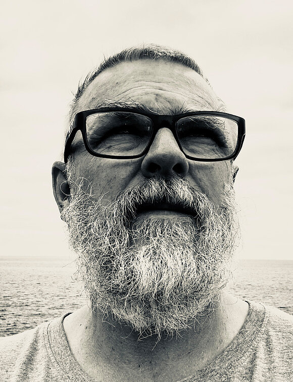 It is a black-and-white portrait of a man with a beard and glasses.