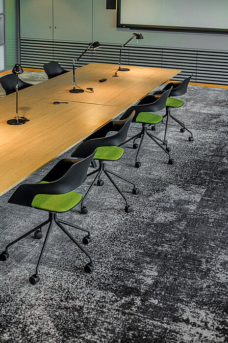 A table setup in a conference room with lamps on top and black Occo chairs arranged around it. The seat pads are green.