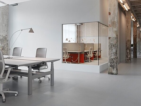 The open workspace combines industrial charm with modern office design. Several AT Mesh units in light gray are on display, blending harmoniously into the minimalist setting. The furniture’s clean lines complement the calm, functional design of the space.