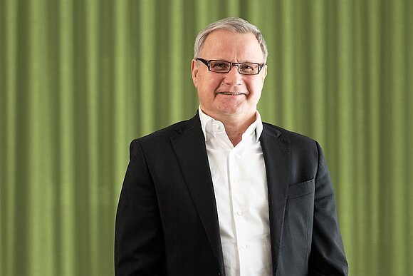 This is a photo of our Advisory Board Chairman Jochen Hahne. He is standing in front of a green curtain.