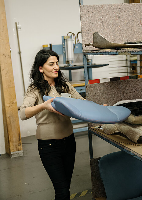Upholsterer Fatma Bayrak is holding a freshly upholstered blue seat shell—designed for an Intra. The scene illustrates the meticulous quality control and the manufacturing process of an ergonomically upholstered component.