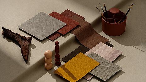 Various fabrics and surfaces in earthy tones are arranged together to serve as a mood board. Objects such as a piece of wood, candles, and a pencil holder in matching colors are also visible.