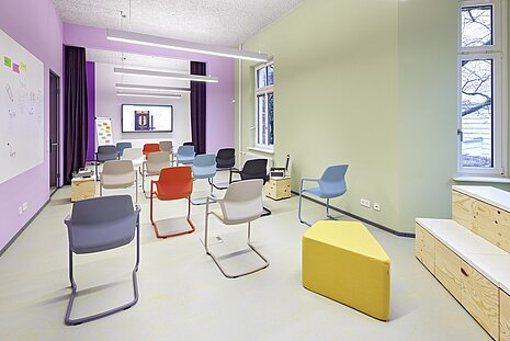 In a very colorful room with purple and green walls, there are many Metrik chairs in various colors. For example, in red, white, beige, black, and gray.