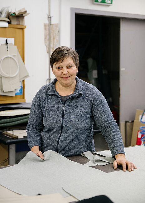 Steffi Stanke, an employee in the upholstery department, is working on fabric cutouts that are likely intended for a Wilkhahn chair. The scene conveys a sense of craftsmanship, precision, and expertise with materials.