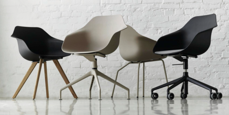 On display are the Yonda chairs in all frame variations: four-star wood and metal, and four-star base with glides. The seat shells are beige and black. They are positioned in front of a white brick wall.