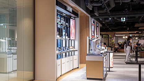 The picture shows a wall cabinet standing in a large room. This open wall cabinet contains various beauty products.
