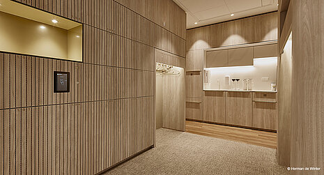 The space has the feel of an elegant coatroom or service area, featuring light wood finishes throughout and integrated lighting. The clean lines and minimalist fixtures create a calm, sophisticated atmosphere.